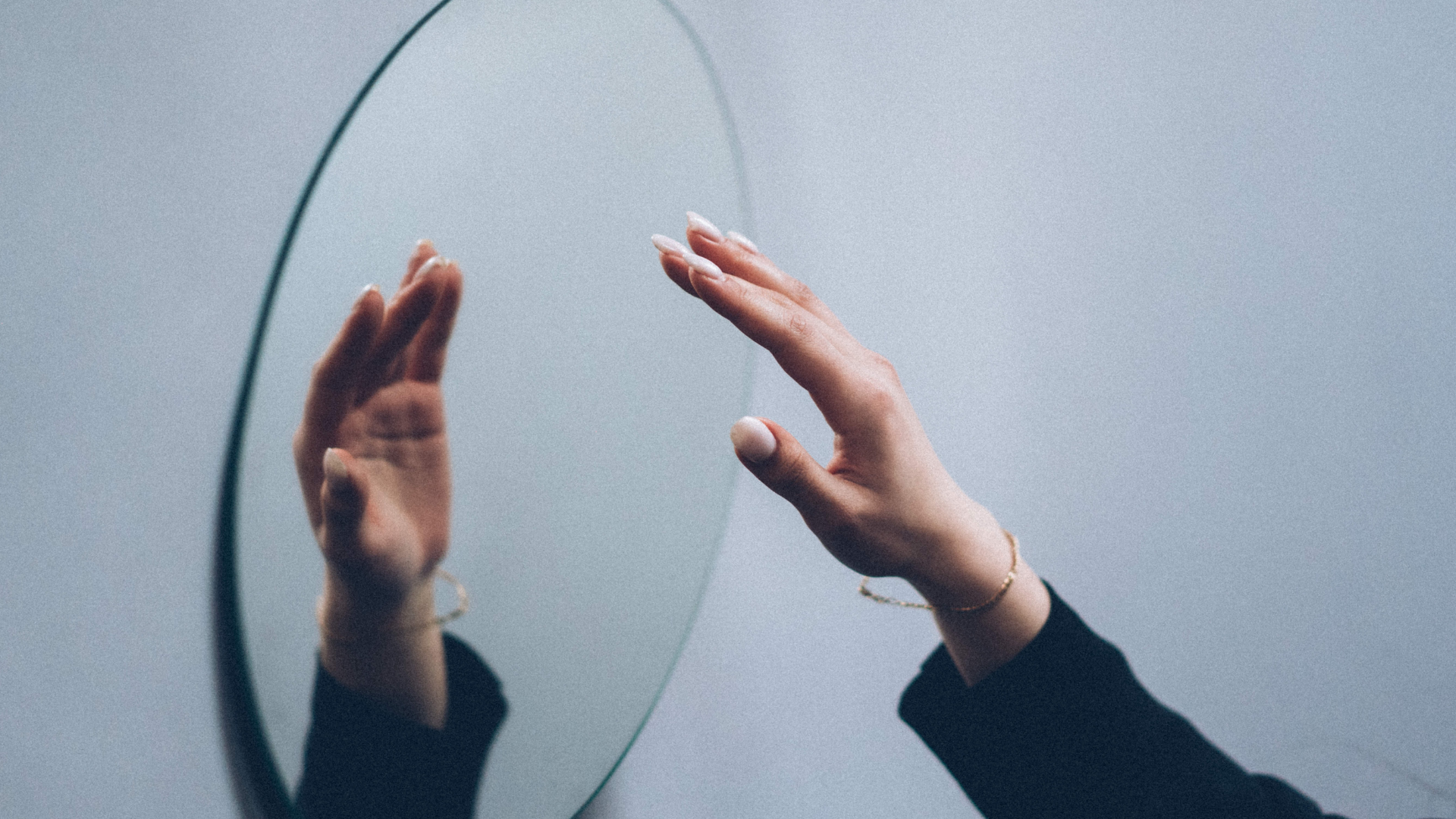 circle mirror hanging on a grey wall and a person's hand reaching up to the mirror