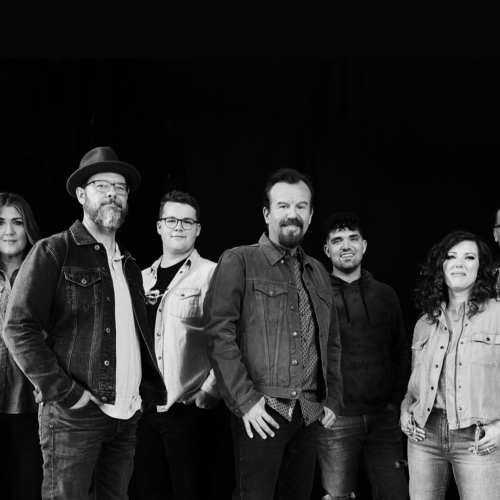 Black and white photo of the seven members of Casting Crowns standing side by side as they smile in front of a black backdrop