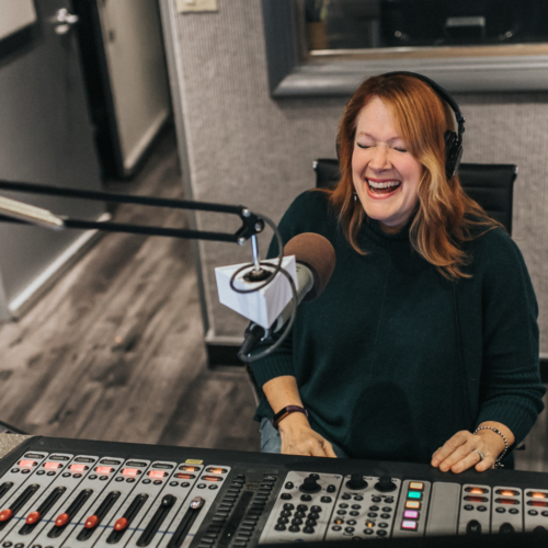 Tracey smiling and laughing as she speaks into a microphone and operates the BRIGHT-FM radio board