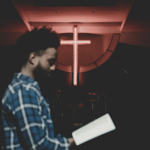 Man standing and reading a Bible as a cross glows in the background