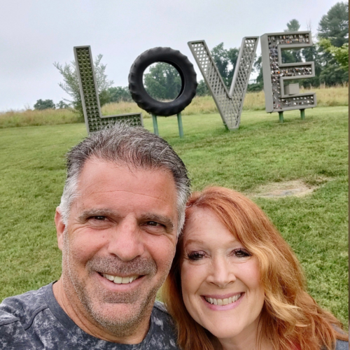 Tracey Tiernan and her husband Gary smiling in front of a sign that spells out LOVE