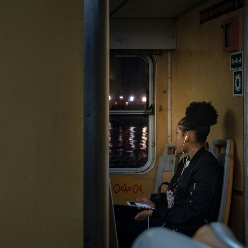woman sitting on a bus staring out the window and listening to music