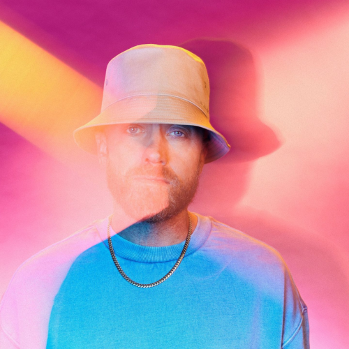 TobyMac wearing a blue shirt in front of a pink background