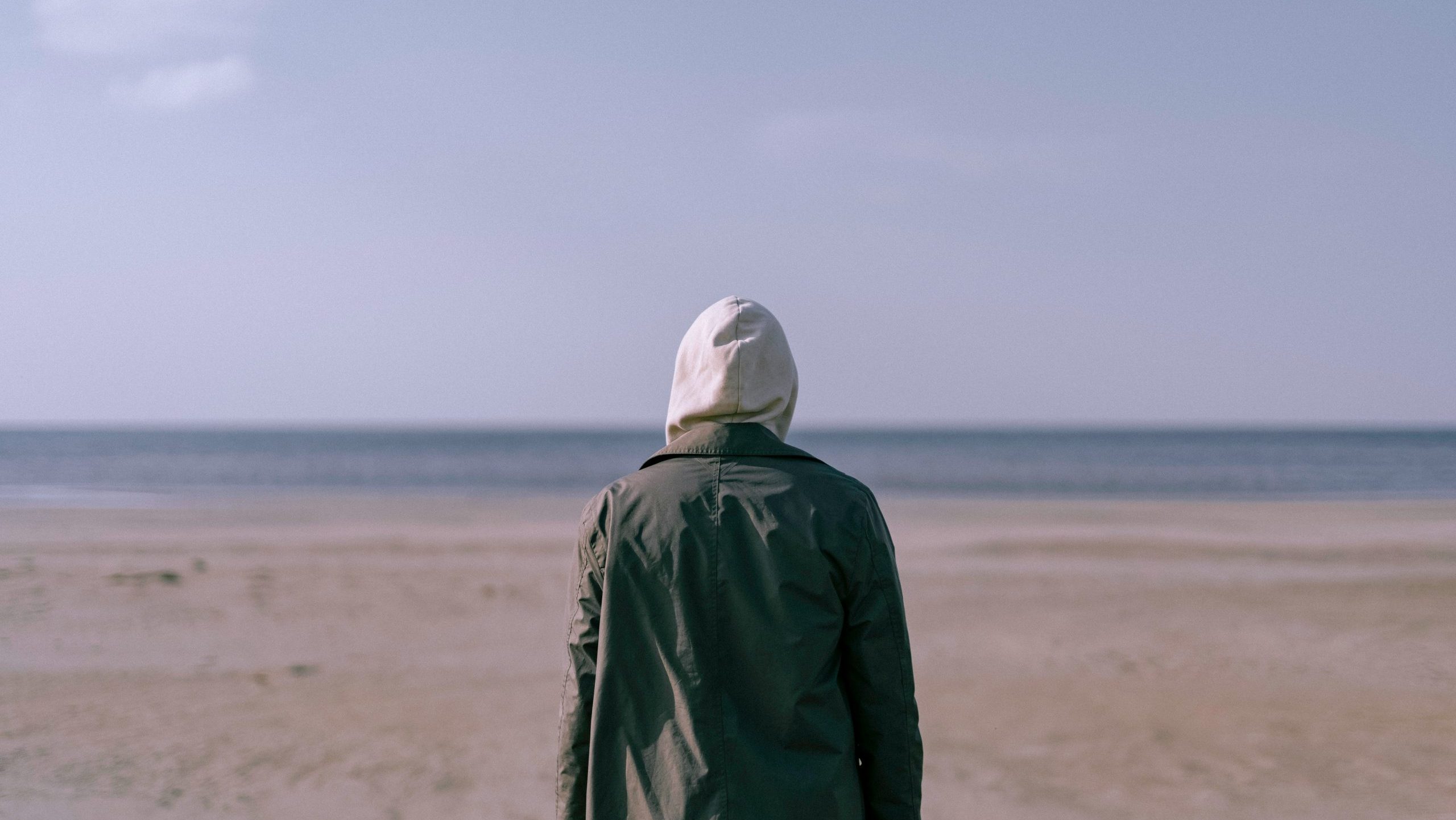 Back of a person with a green jacket looking at the sea on a beach.